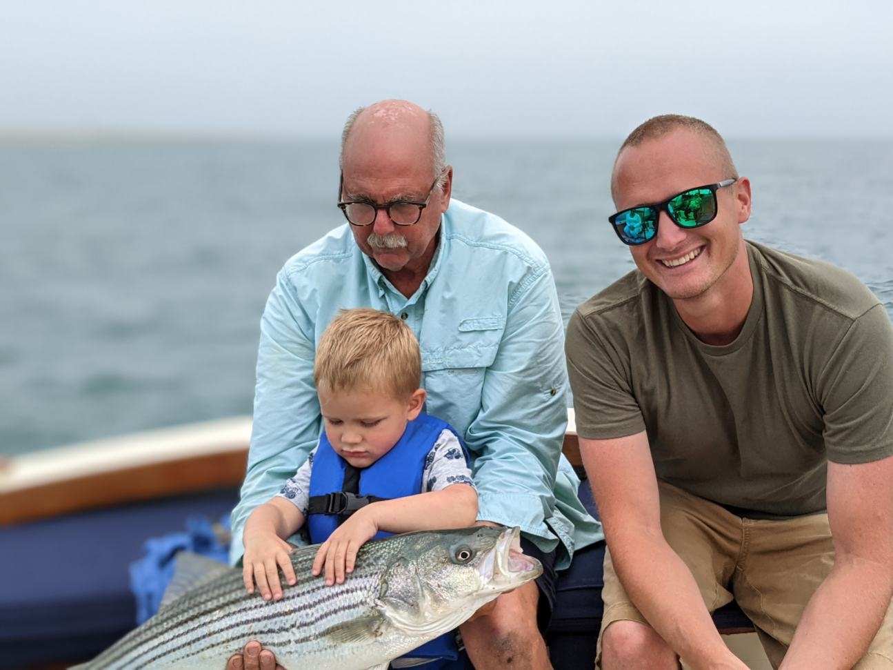 Three generations posing with a big striper caught aboard The Beth Ann in Provincetown