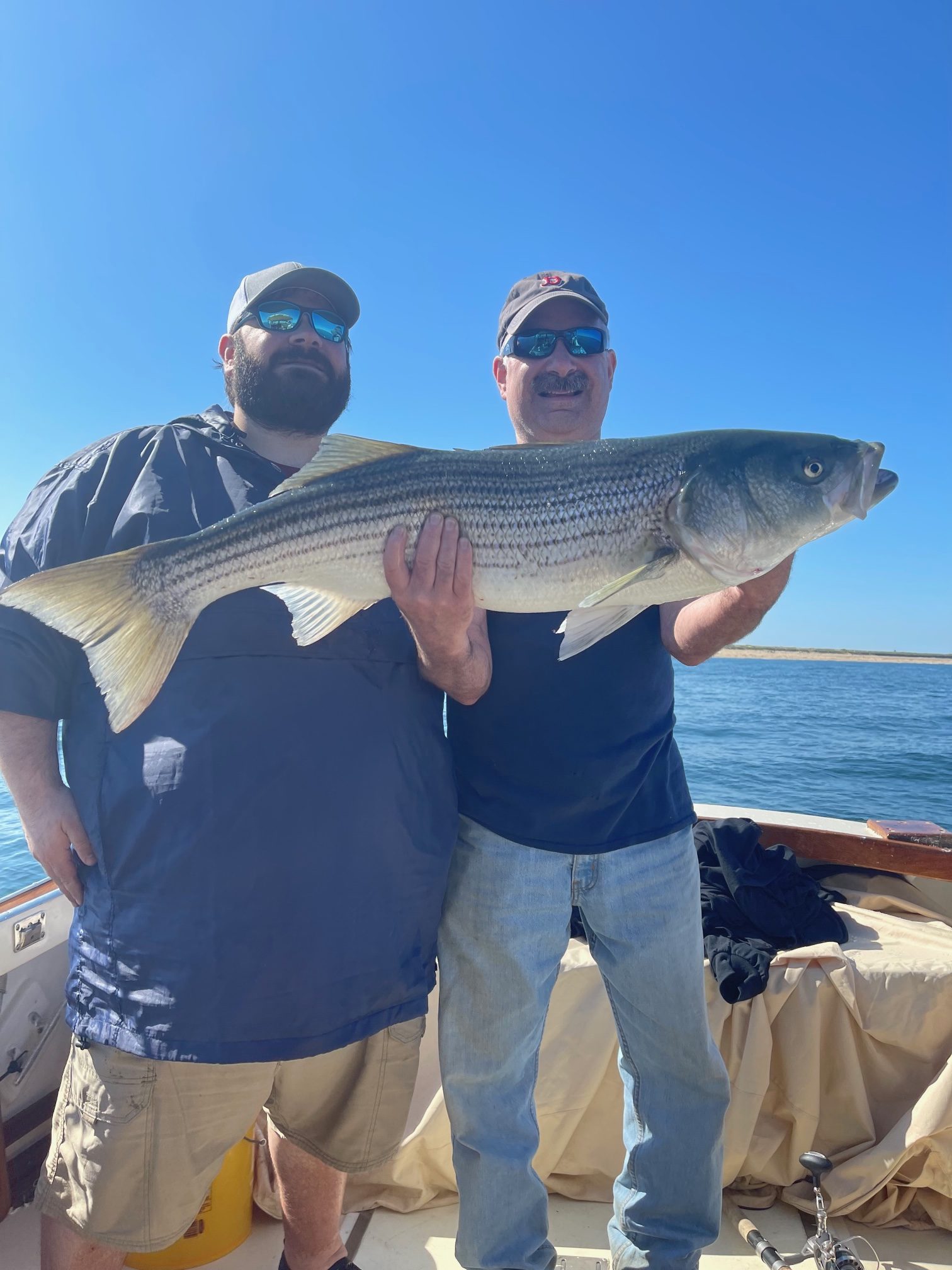 Customers holding a large striped bass caught aboard the Beth Ann