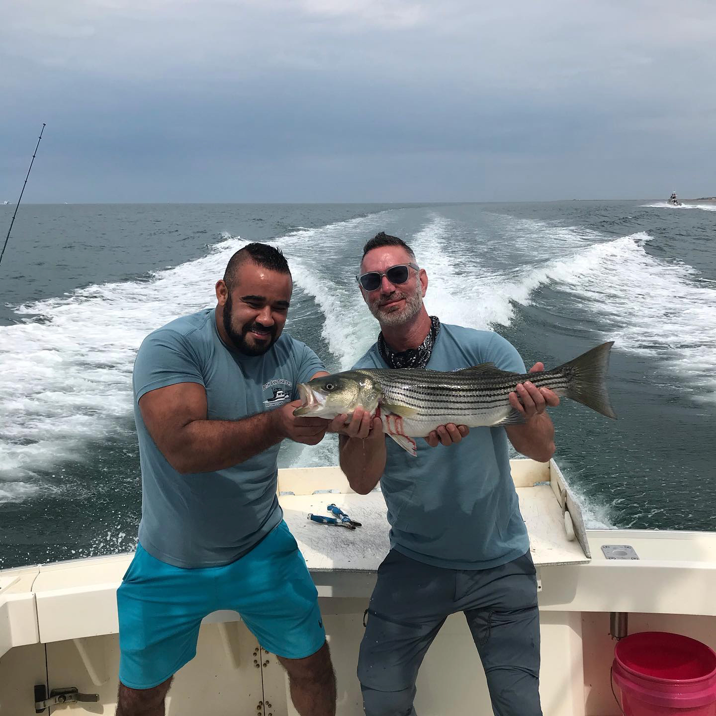Two very excited customers holding a striper just caught on board The Beth Ann in Provincetown