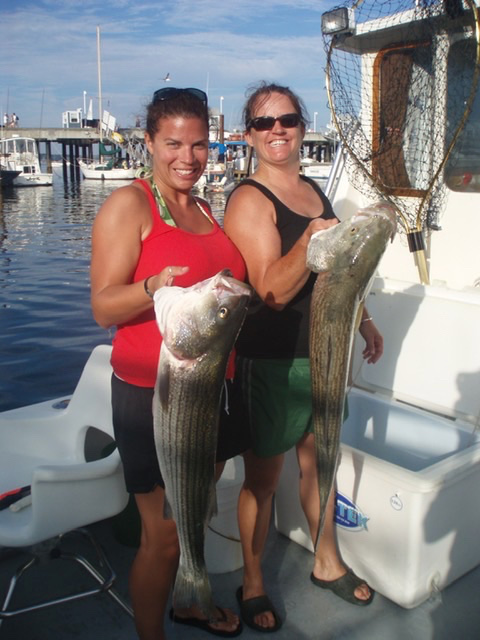 Two women holding large stripers caught on board The Beth Ann during a fishing charter in Provincetown]