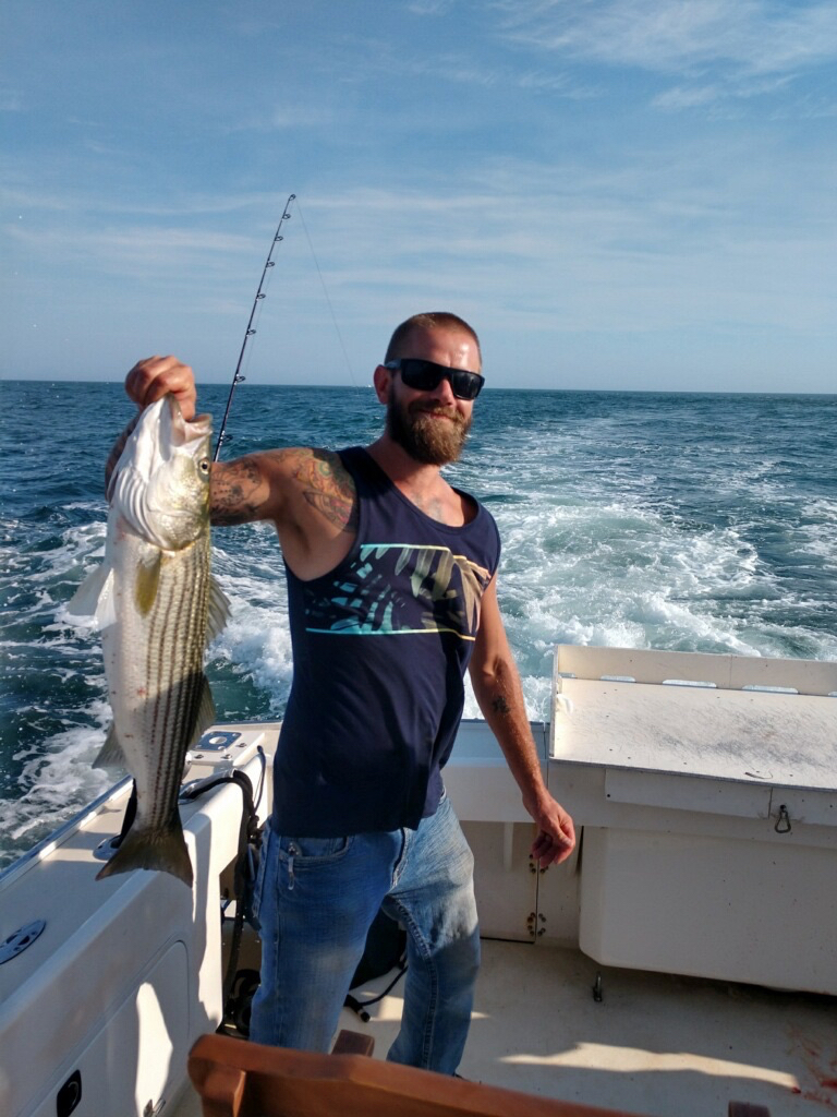 A customer holding a nice striped bass caught aboard The Beth Ann on a Fishing Charter trip