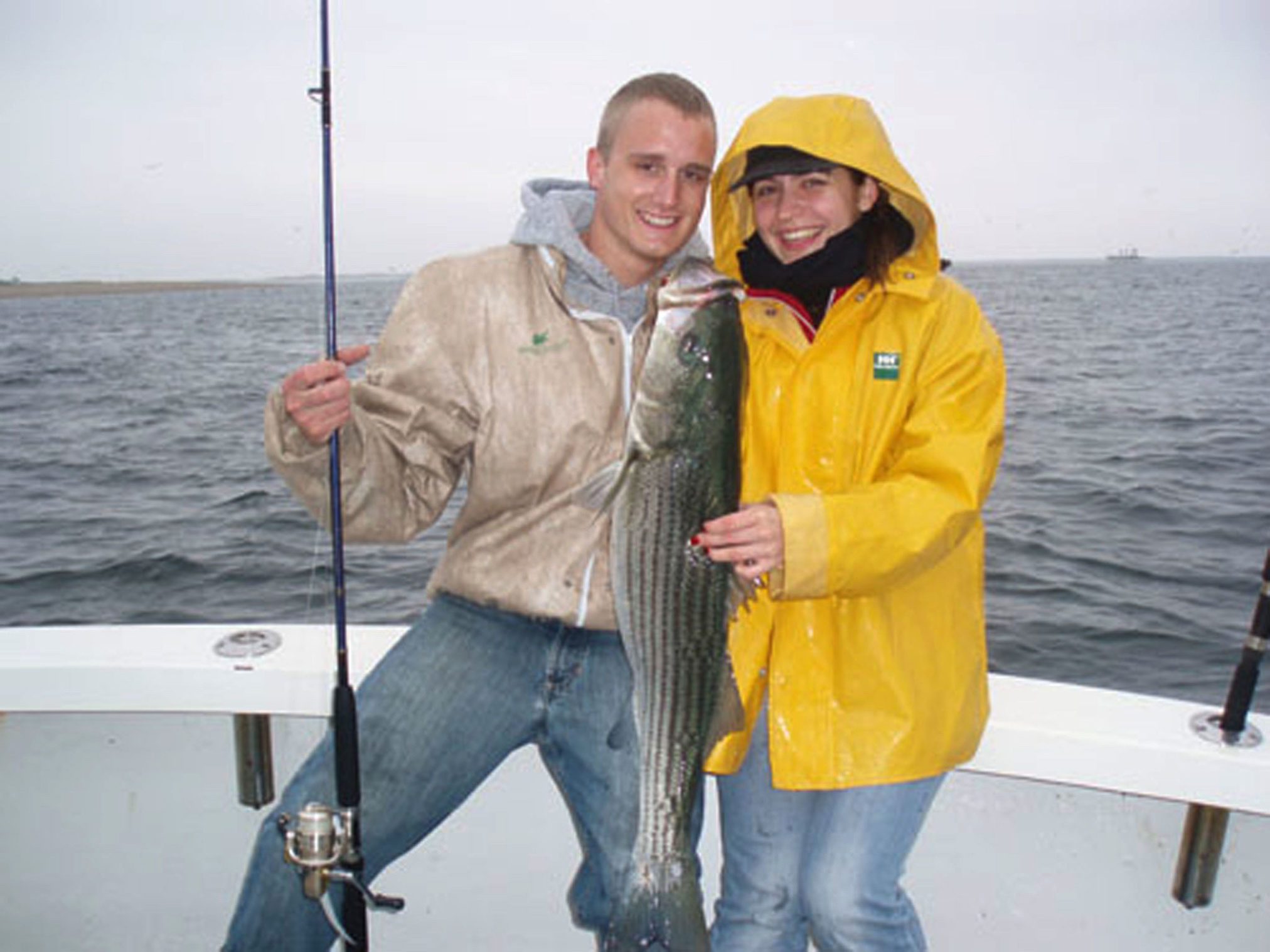A happy couple holding a striped bass caught aboard The Beth Ann during a fishing charter