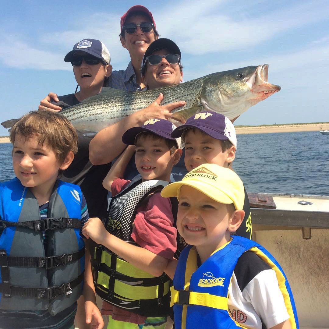 Large family holding a striper caught on a family fishing charter trip